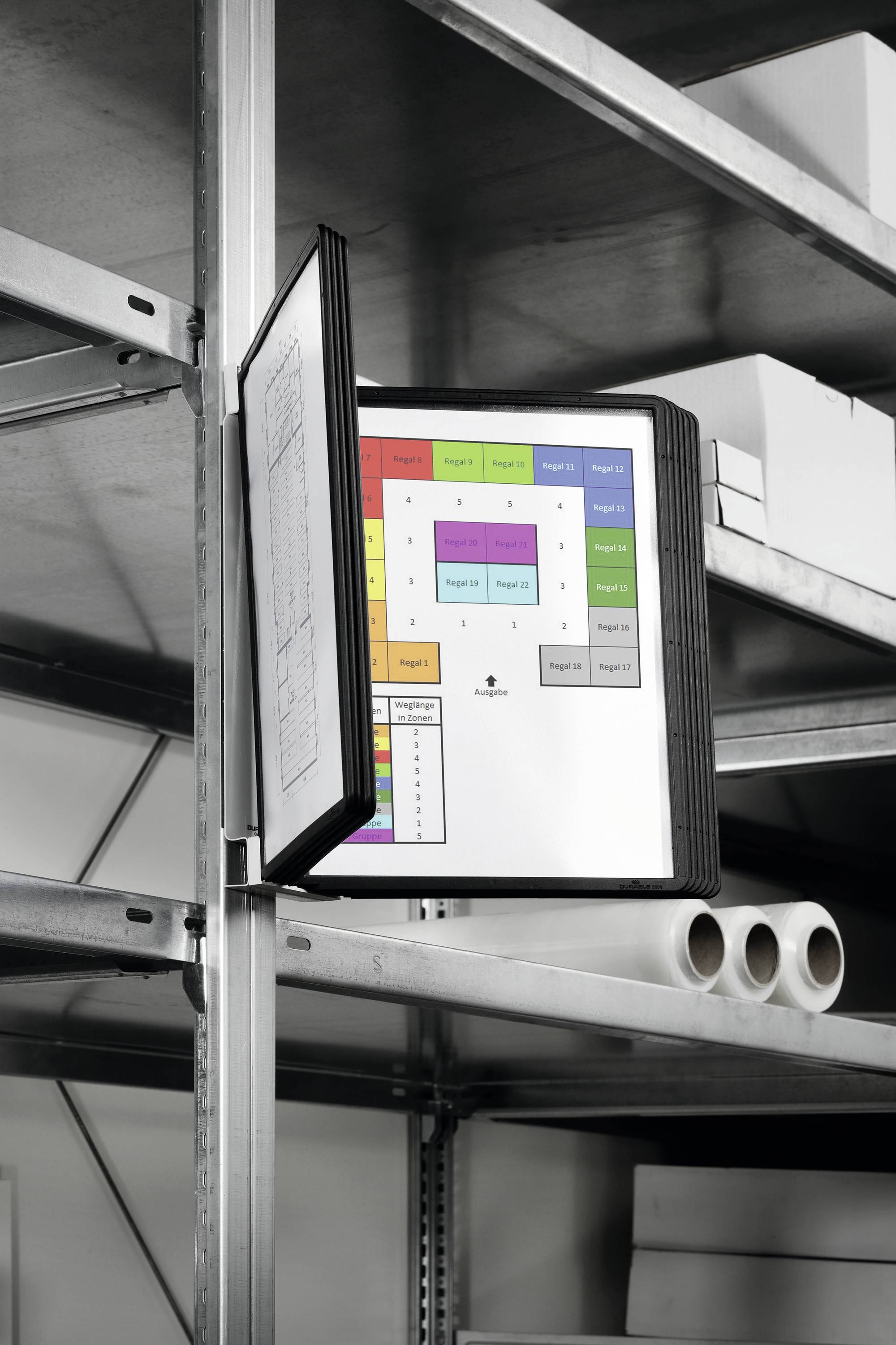 Otvorená mapa s farebnými diagramami visí na polici. Dolu pod ňou ležia viaceré rolky papiera a kartóny.