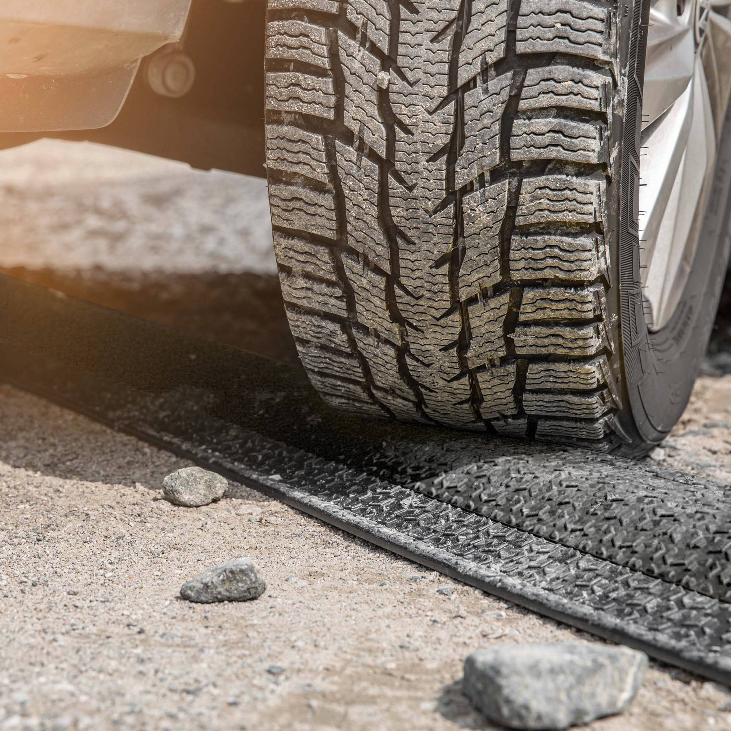 Detailný záber pneumatiky automobilu na prašnej ceste, ktorá zanecháva prudké stopy po brzdení alebo zrýchlení. Kamene sú roztrúsené okolo týchto stôp.