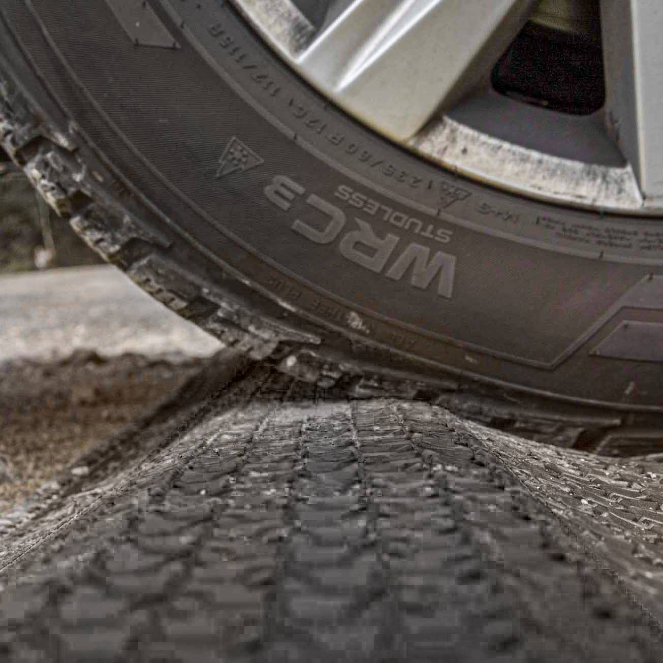Detailný záber pneumatiky automobilu na nerovnej ceste. Pneumatika má výrazné dezény a je čiastočne opotrebovaná.