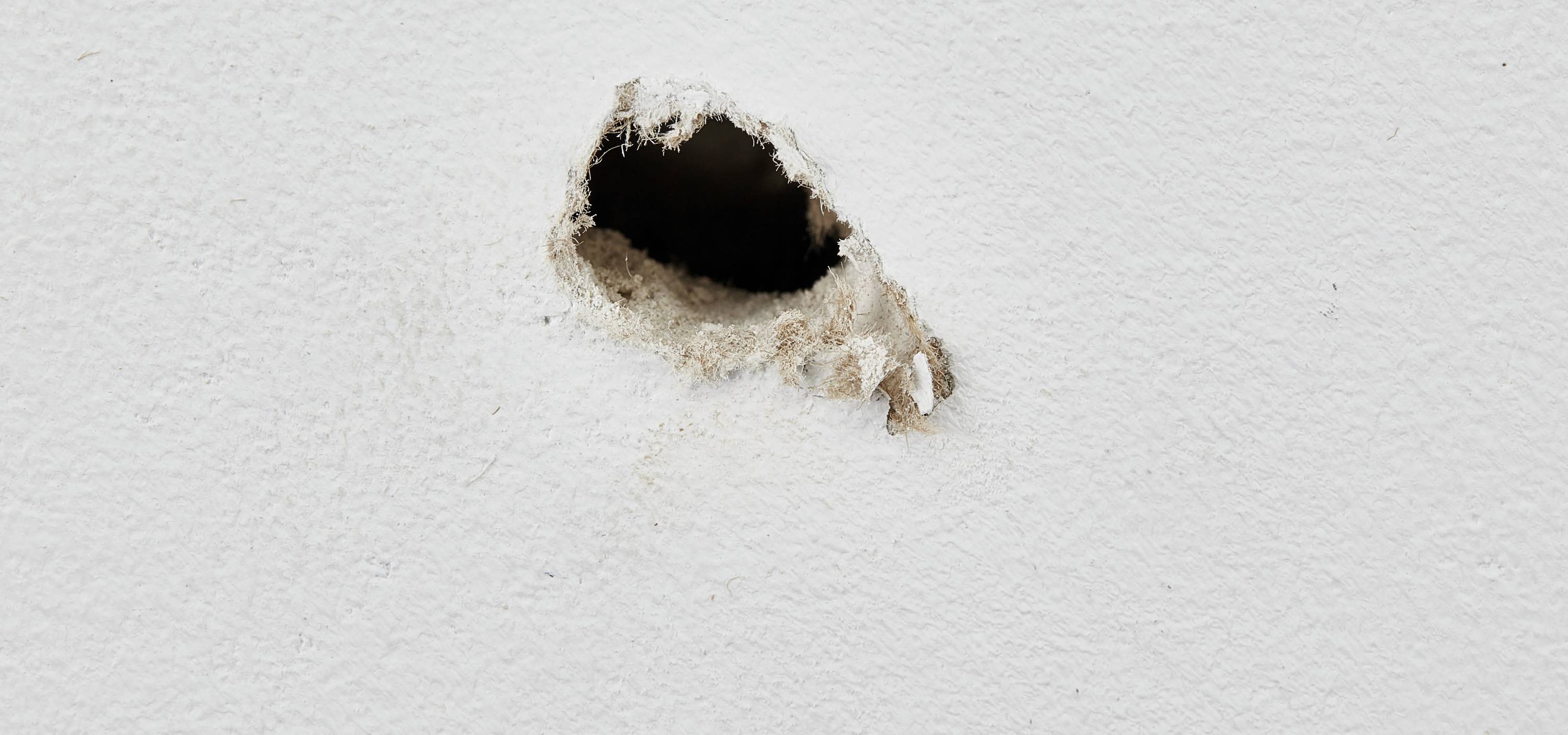 Veľká diera v bielej stene, odhaľujúca vnútorný materiálový priestor.