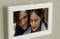 Na stene visí zarámovaná fotografia s dvoma usmiievajúcimi sa osobami, ktoré sedia blízko seba.