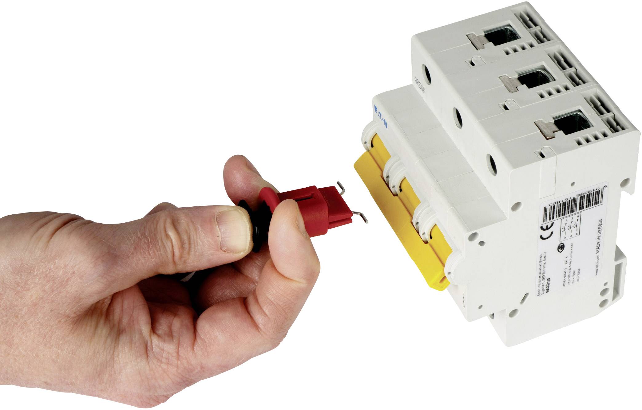 Ruka drží červený testovací adaptér smerujúci k bielemu elektrickému ochrannému spínaču s tromi spínačmi.