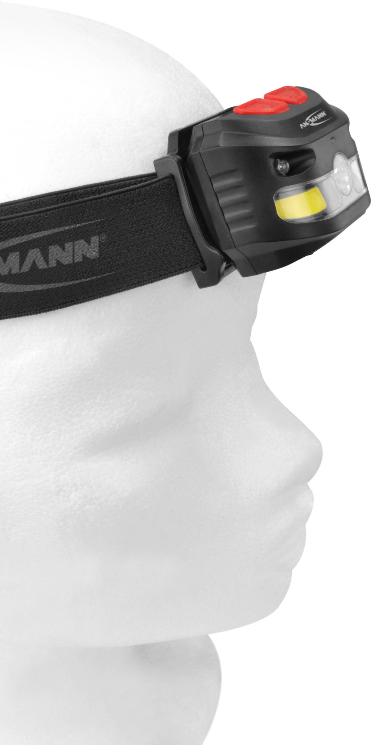 Modelová hlava nesie čiernu čelovú lampu s červeným tlačidlom, pohľad z boku. Lampa je pripevnená na čiernom páse.