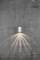 Malá, moderná kovová nástenná lampa vrhá jemné svetlo na drsnatú sivú betónovú stenu. Svetelné lúče sa rozptyľujú vejárovitým tvarom.