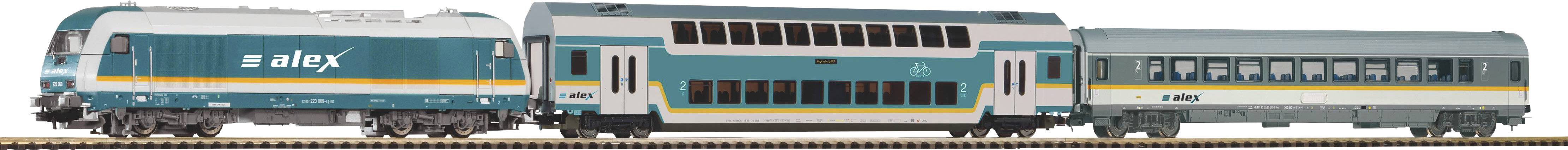 Modrobiely osobný vlak s tromi vozňami ide po koľaji, pričom jeden z vozňov je poschodový odťahový vozeň.