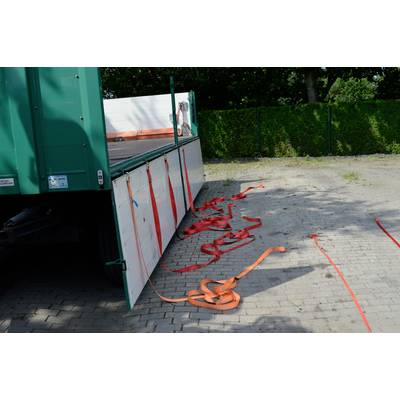 Nákladné auto s otvorenými bočnými stenami na dláždenej ploche dvora. Niekoľko červených a oranžových popruhov leží na zemi.