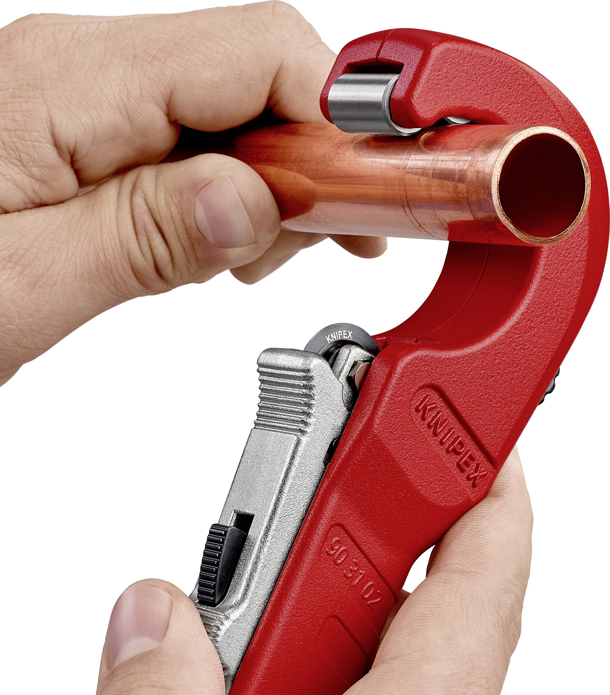 Jedna ruka drží červený rezač rúr, ktorý prechádza cez medené potrubie.