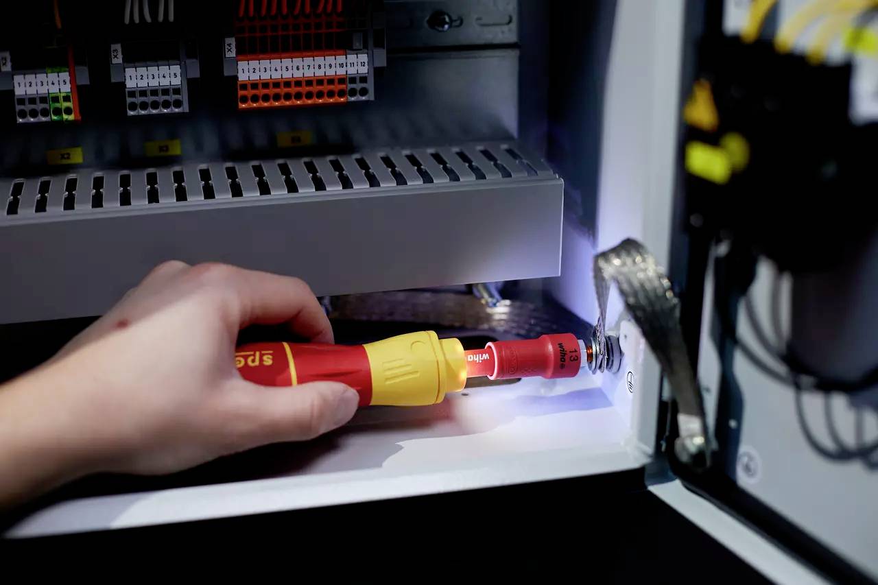 Ruka s krížovým skrutkovačom upevňuje skrutku v elektrickom rozvádzači. Káble a prípojky sú viditeľné.