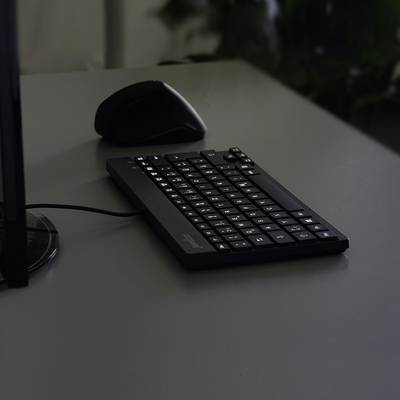 Na tmavom stole ležia čierna bezdrôtová klávesnica a myš vedľa monitora.