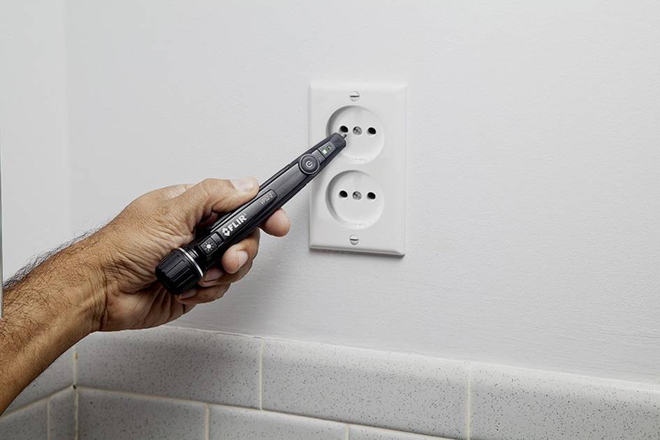 Jedna ruka drží skúšačku napätia pri elektrickej zásuvke, aby skontrolovala elektrický prúd.