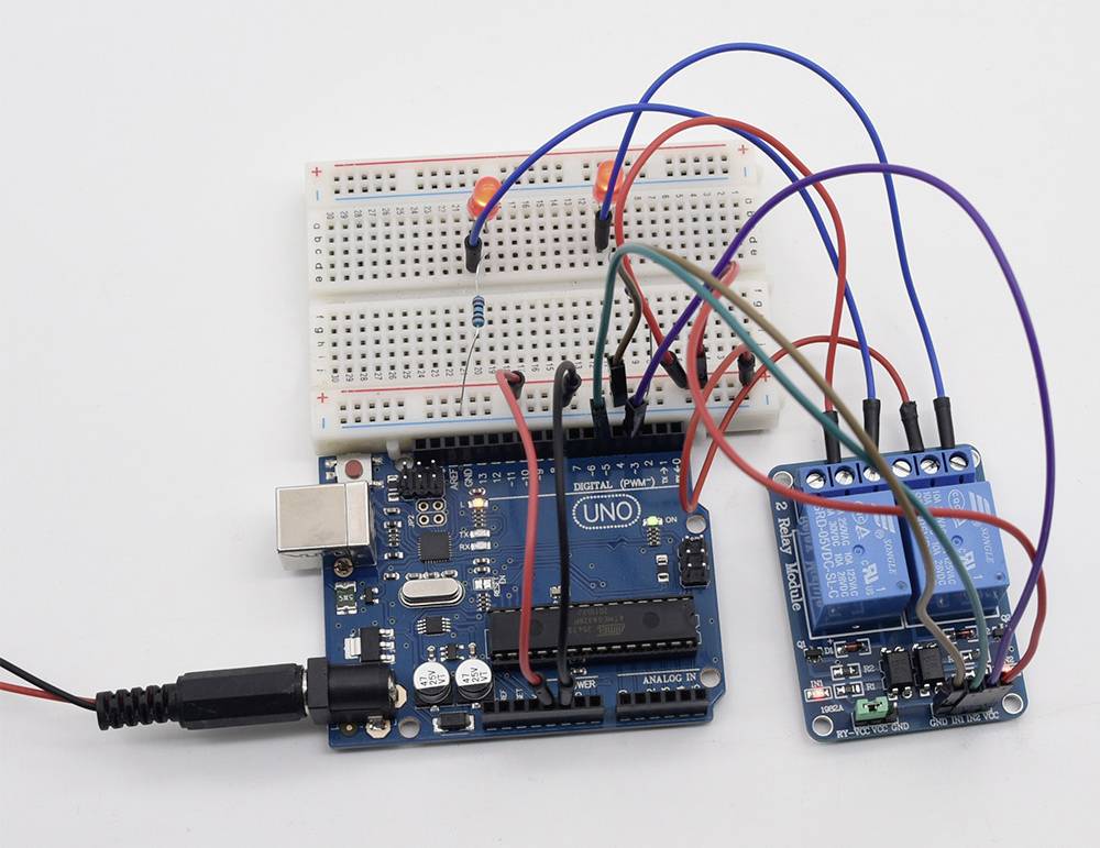Arduino set s nepájacou doskou, prepojovacími vodičmi a relé modulom. Nepájacia doska je pripojená k LED diódam a odporu, všetky komponenty sú elektricky prepojené.