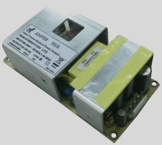 Otvorený napájací zdroj s viditelnými elektronickými komponentmi na doske plošných spojov vrátane kondenzátorov a transformátora.