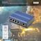 Priemyselný 4-portový gigabitový PoE switch pred priemyselnou scénou s dymom a plameňmi v pozadí, produkt spoločnosti 'Digitus'.