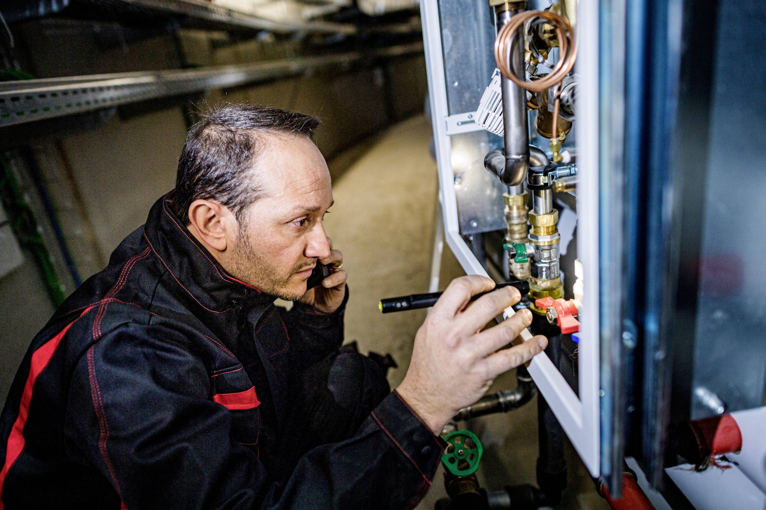 Technik kontroluje vnútorné mechanizmy vykurovacej sústavy vreckovou lampou v technickej miestnosti.