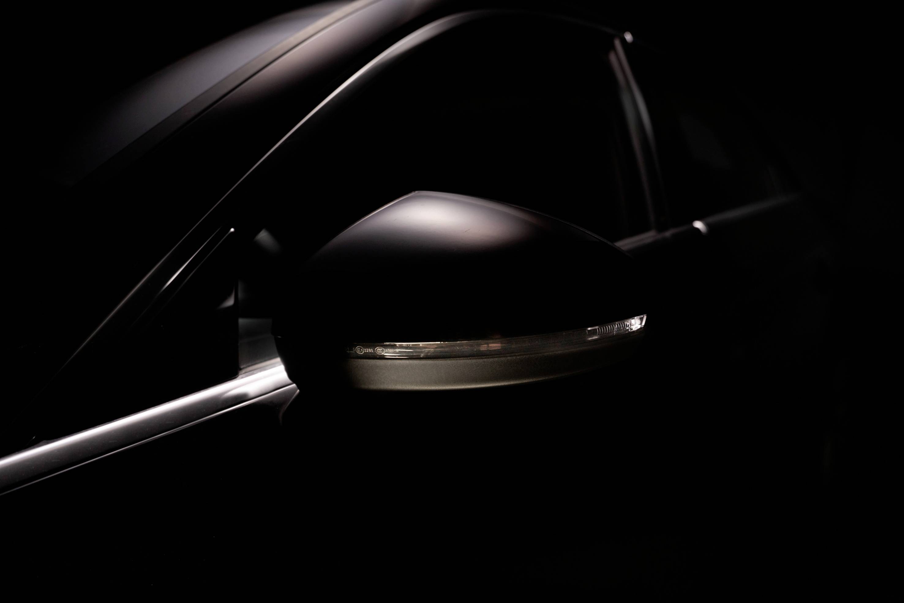 Detailný záber spätného zrkadla automobilu v tlmenom svetle, ktorý odhaľuje tmavý dizajn a elegantné línie vozidla.