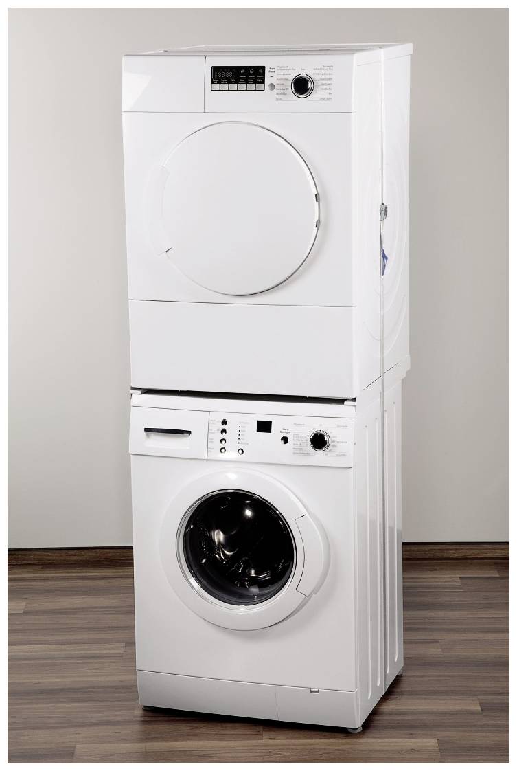 Práčka a sušička v bielej farbe, uložené na seba na drevenej podlahe pred neutrálnou stenou.