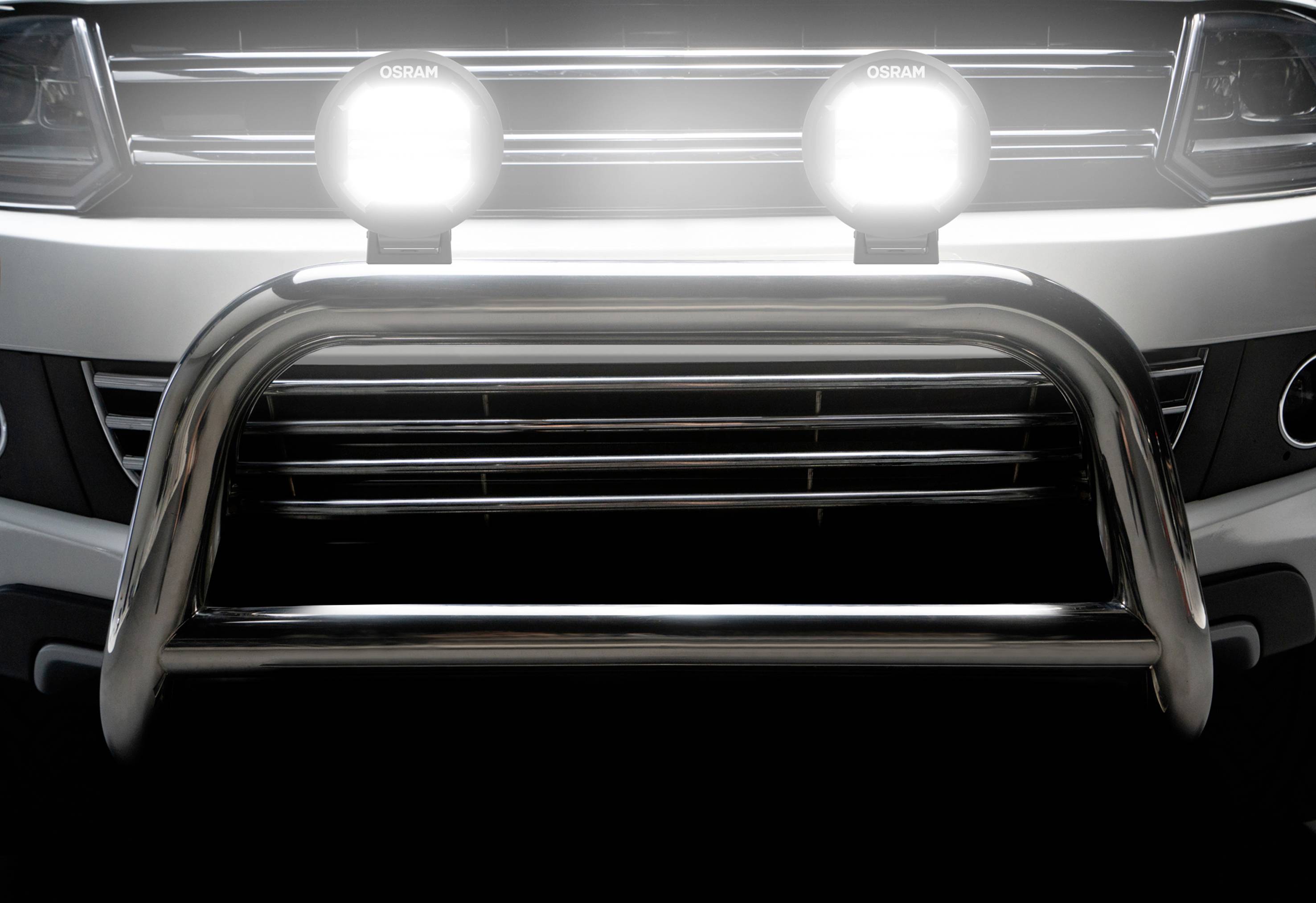 Svetlý predný nárazník vozidla s dvoma svietiacimi svetlometmi a stabilným kovovým oblúkom, ktorý poskytuje dodatočnú ochranu.