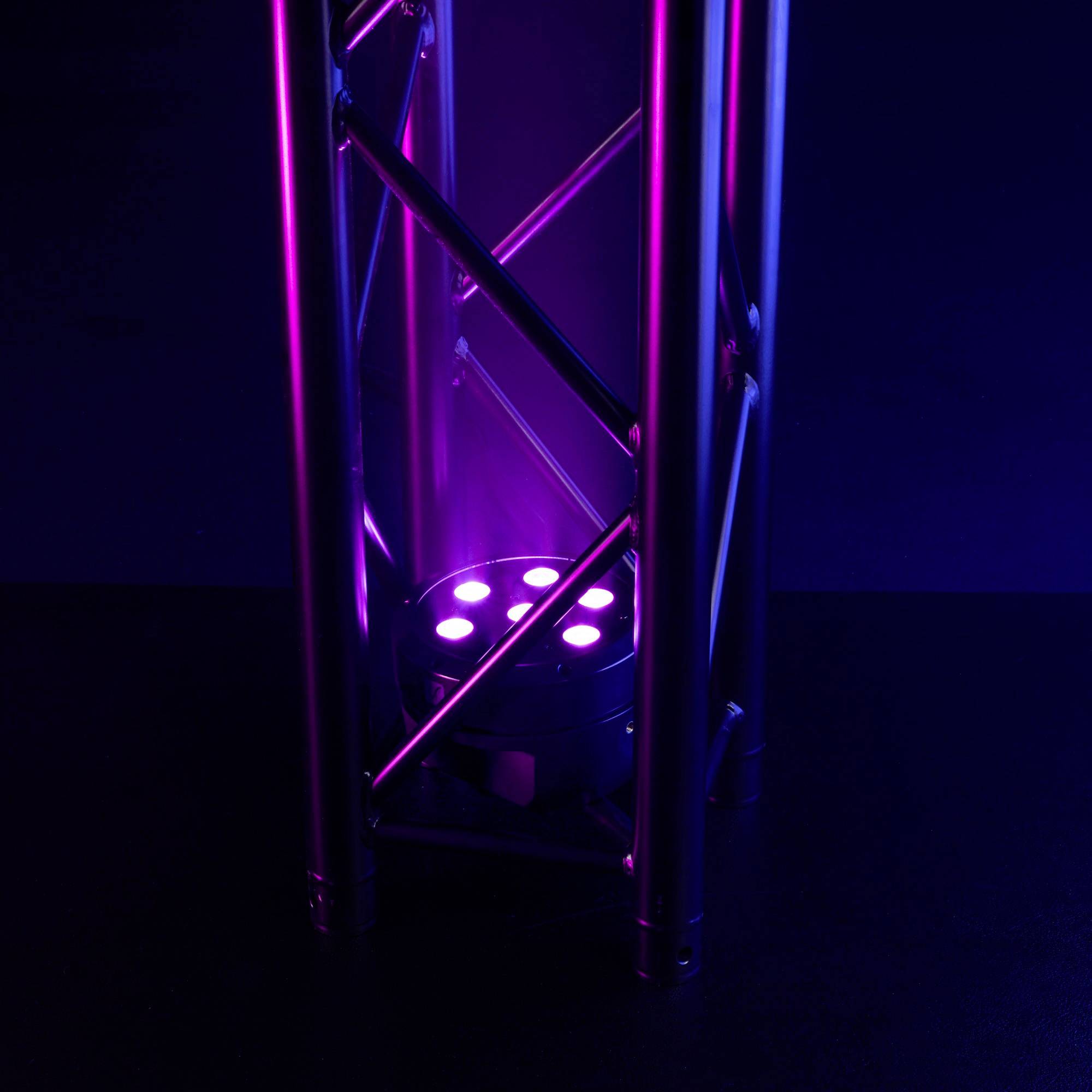 Kovová štruktúra s fialovým svetlom, ktoré vyžaruje bodový reflektor umiestnený na zemi. Tmavé pozadie zvýrazňuje osvetlenú štruktúru.