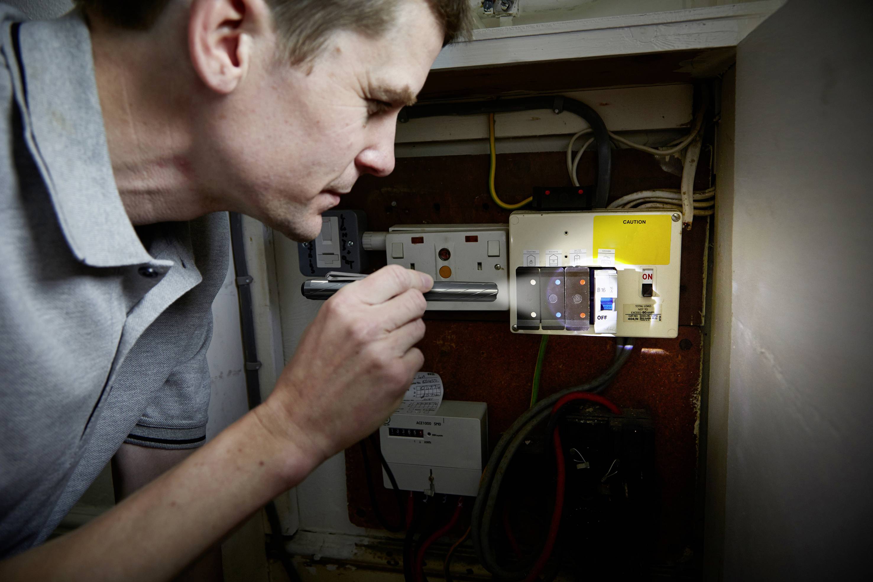 Muž kontroluje elektrický rozvádzač. Osvetľuje zariadenie baterkou, aby skontroloval zapojenie.