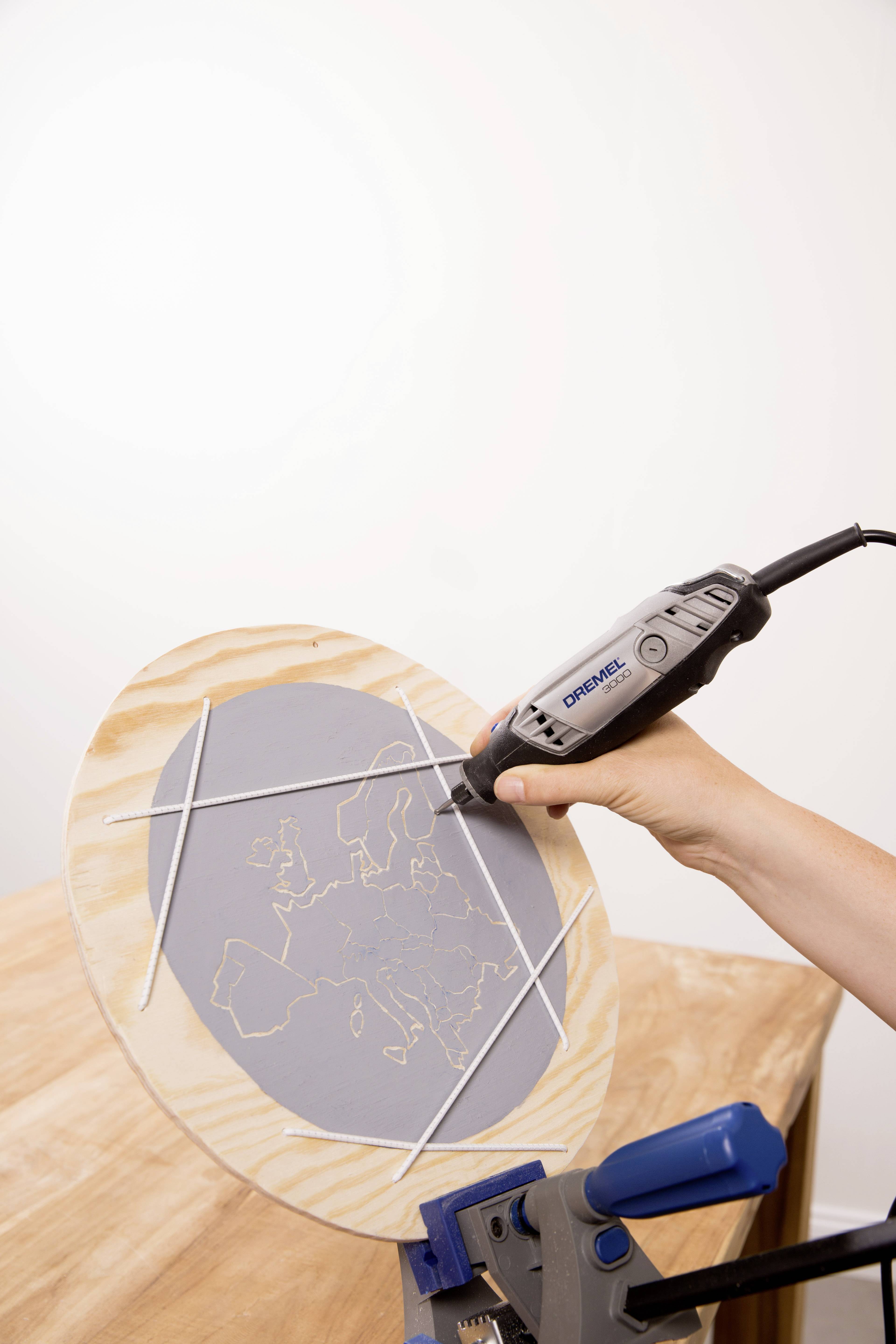 Osoba používa nástroj Dremel na vyrezávanie mapy Európy do drevenej dosky.