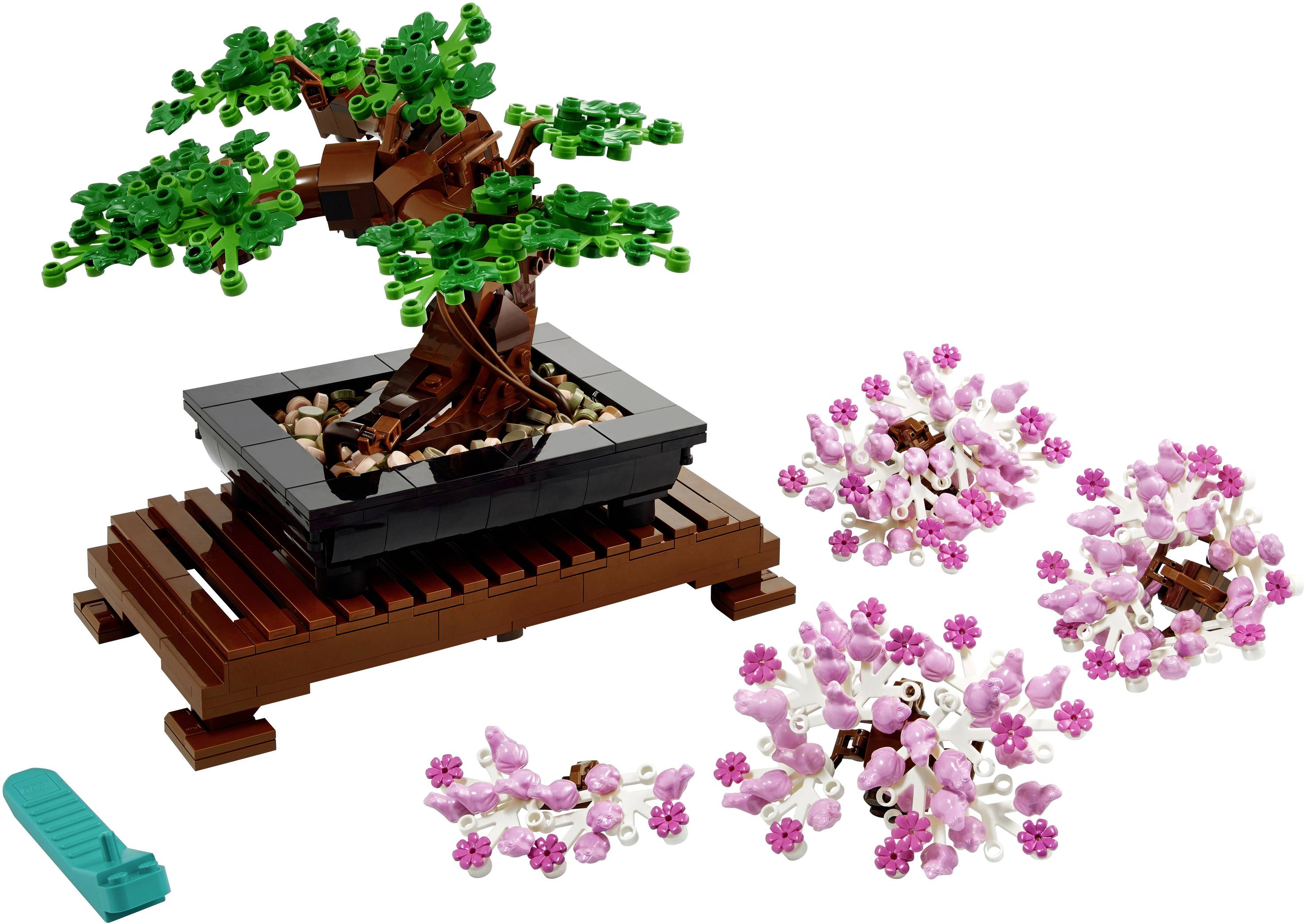 LEGO bonsaj strom s vymeniteľnými zelenými a ružovými listami stojí na drevenej podložke. Vedľa leží nástroj.