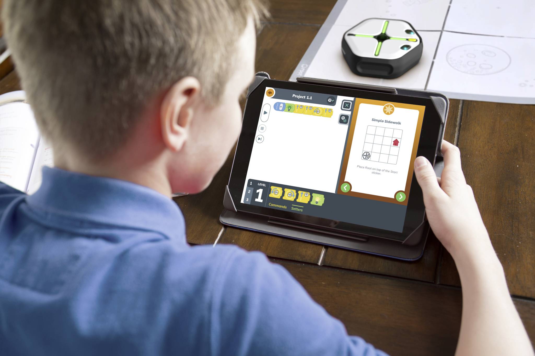 Dieťa drží tablet, na ktorom je zobrazená vzdelávacia aplikácia s koordinačným systémom. Malý robot leží na stole.