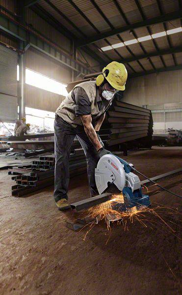 Robotník v ochrannom oblečení rezá kovové potrubia rozbrúskou v továrenskej hale, pričom okolo lietajú iskry.