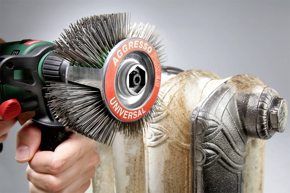 Drôtená kefa sa používa na odstránenie hrdze z vykurovacieho telesa. Akcia ukazuje čistenie starého kovového predmetu.