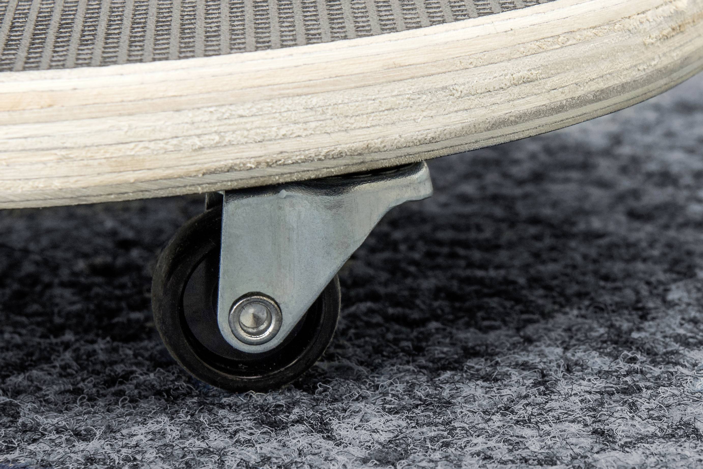 Detailný záber skateboradru s malým čiernym kolieskom na sivom koberci.