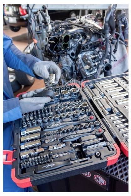 Rukavice mechanika trieďia náradie - zásuvky a kľúče vedľa rozloženého automotormu v dielni.