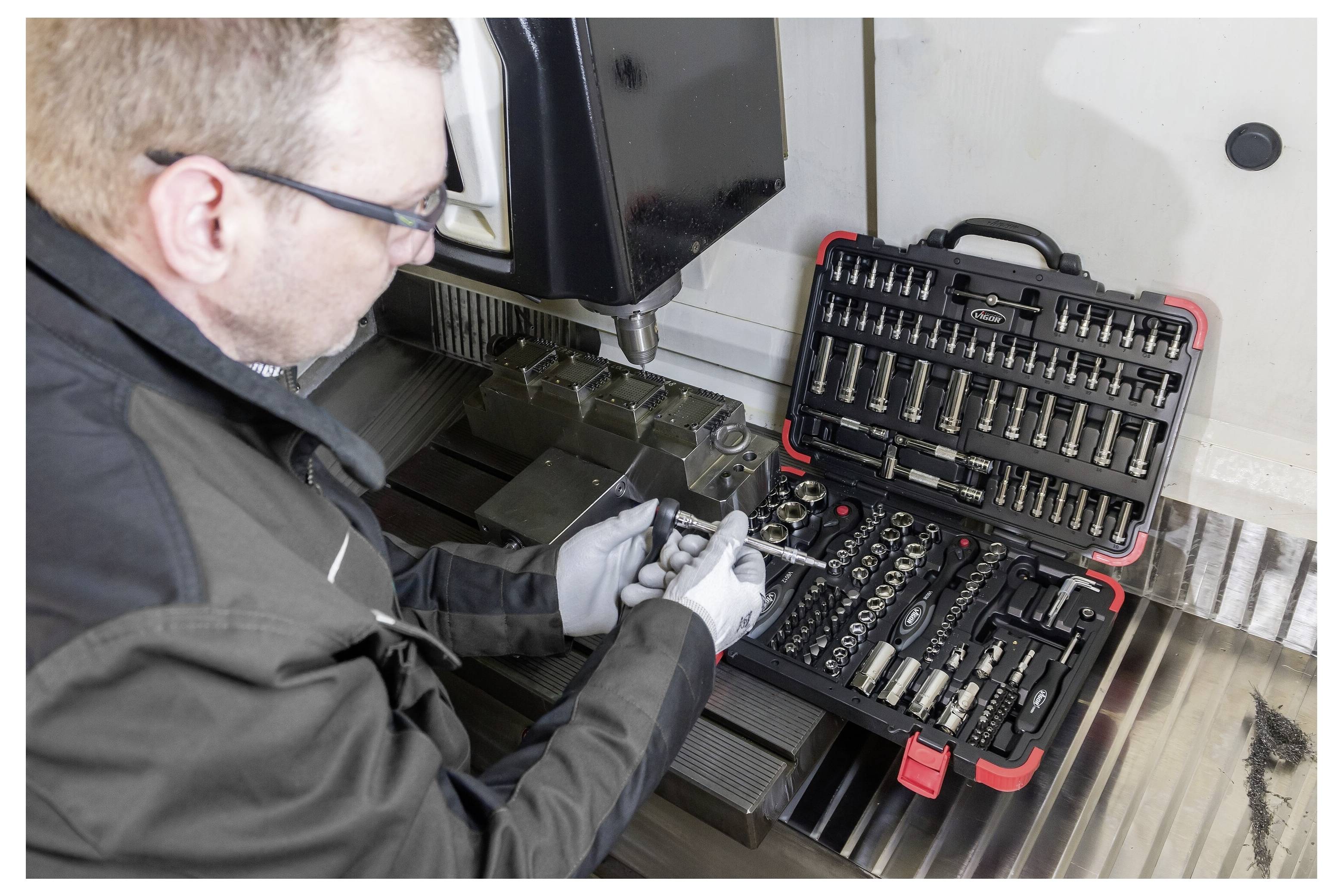 Technik používajúci sadu skrutkovacích klúčov a kľúčov na prácu s kovovým strojom v priemyselnej dielni.