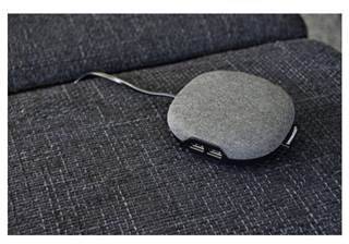 Sivý, okrúhly USB hub s dvoma portami a káblom leží na tmavosivom poťahu sedačky.