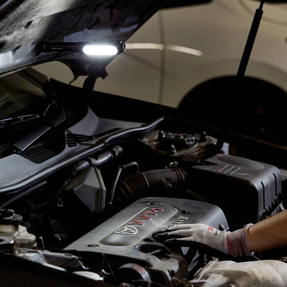 Mechanik pracuje na motore automobilu v dielni, kapota je otvorená.