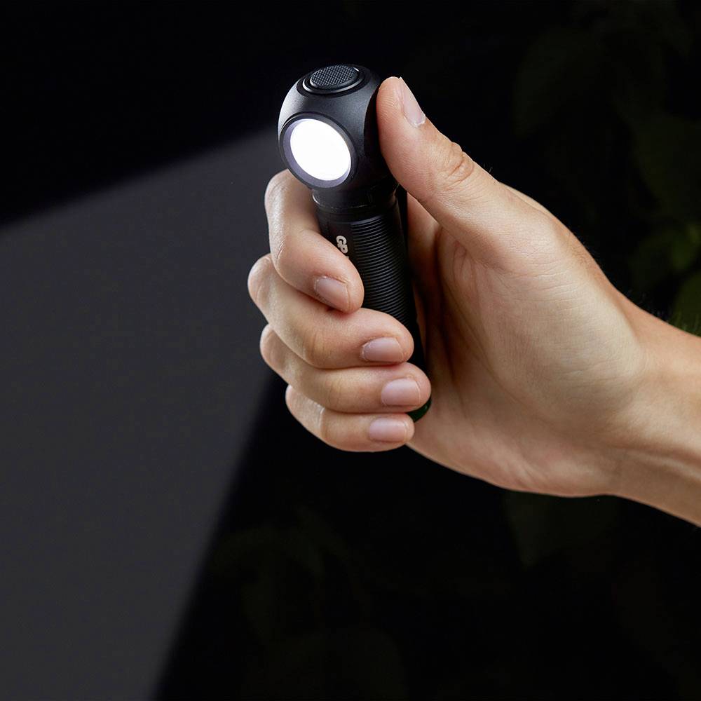 Ruka drží zapnutú malú baterku pred tmavým pozadím.
