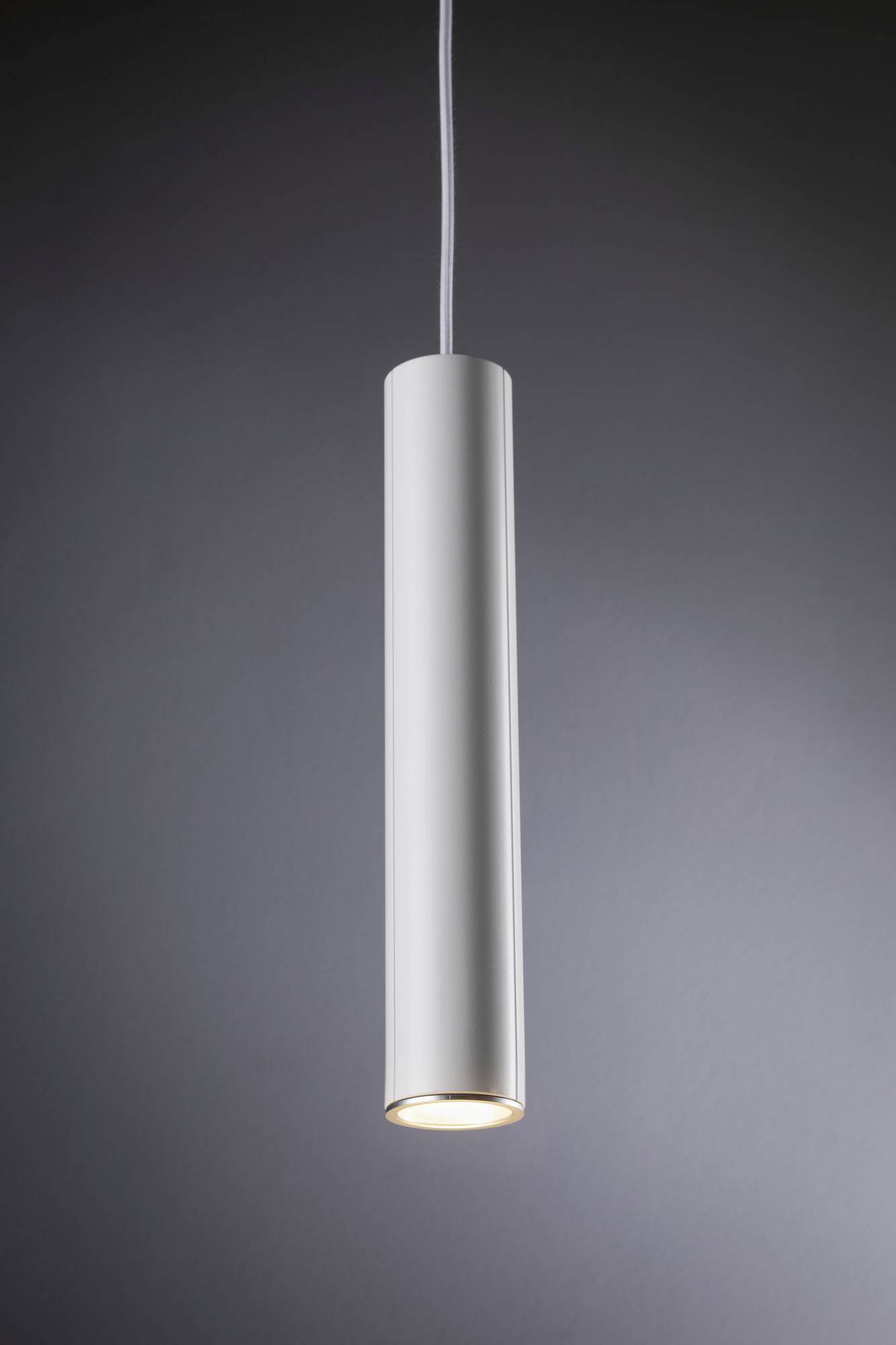 Valcovitá biela závesná lampa svieti zhora v slabo osvetlenej miestnosti.