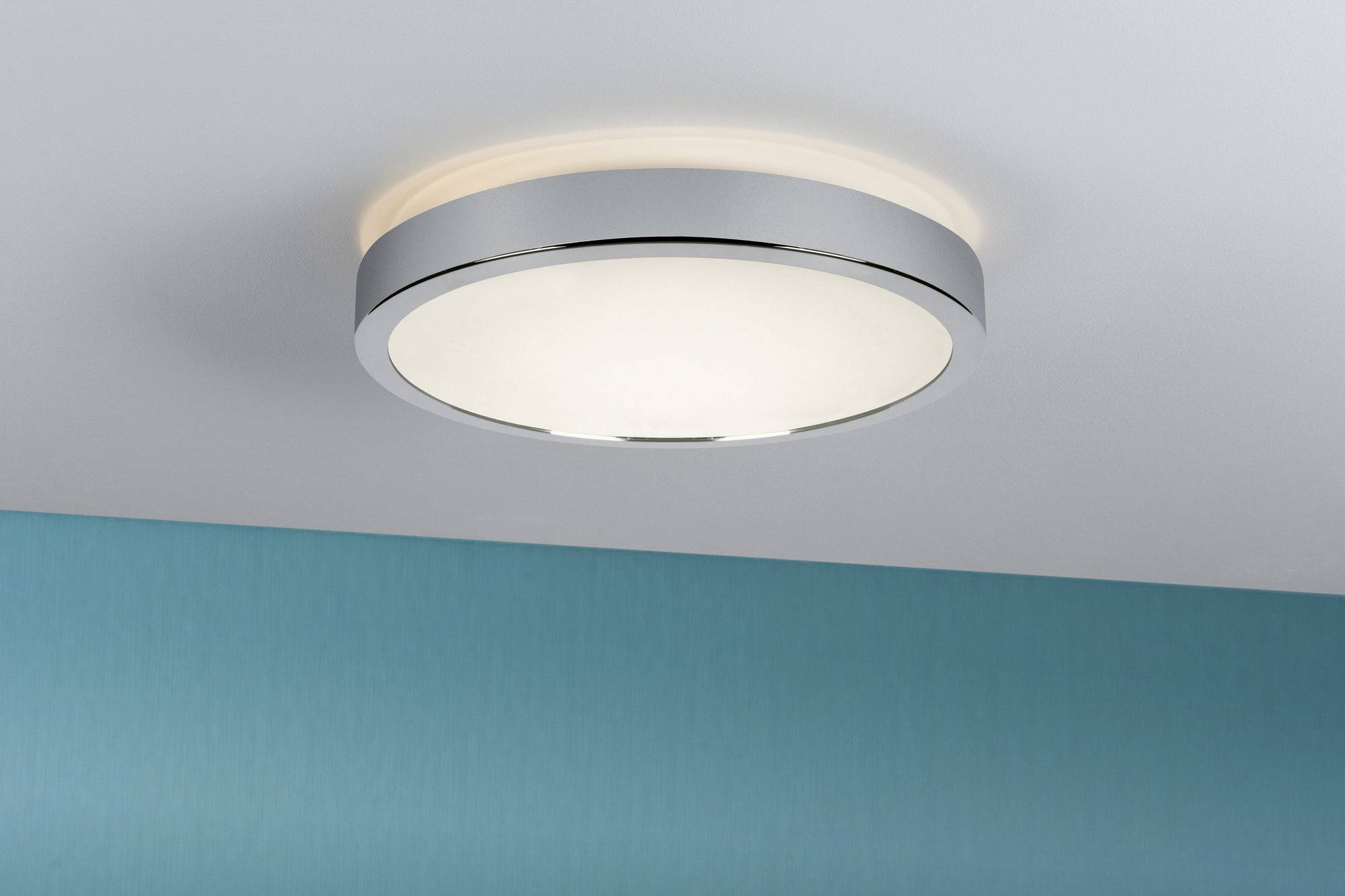Okrúhle stropné svietidlo s kovovým rámom a matným sklom visí na bielo-modrom strope a vytvára jemné ambient svetlo.