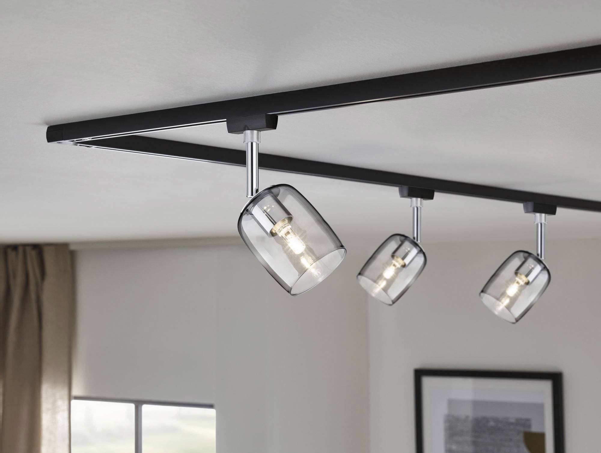 Tri moderné stropné lampy s nastaviteľnými tienidlami upevnené na čiernej lište, namontované na bielom strope miestnosti.