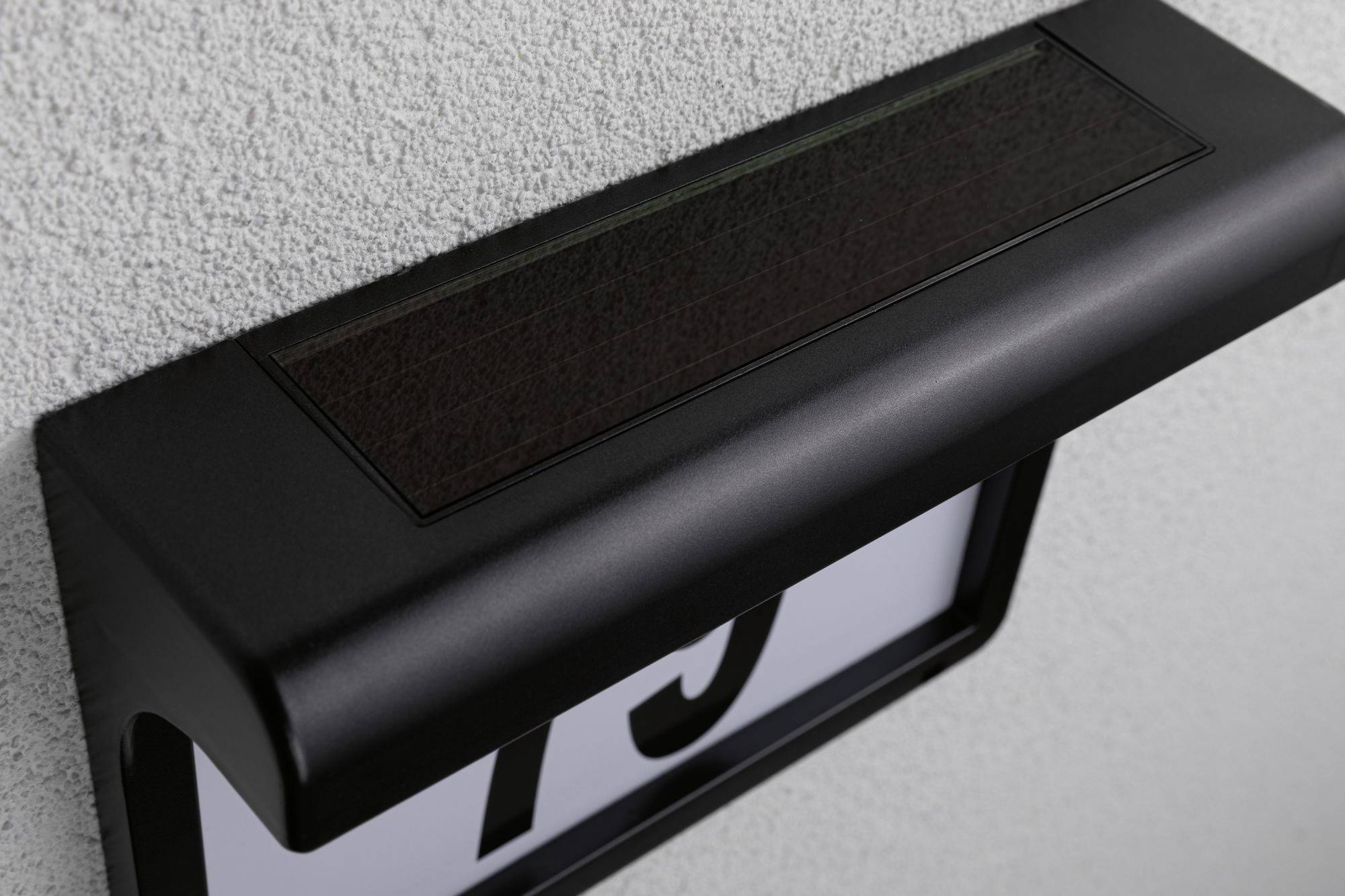 Čierne solárne domové číslo, namontované na sivej stene, zobrazuje číslo '79'.