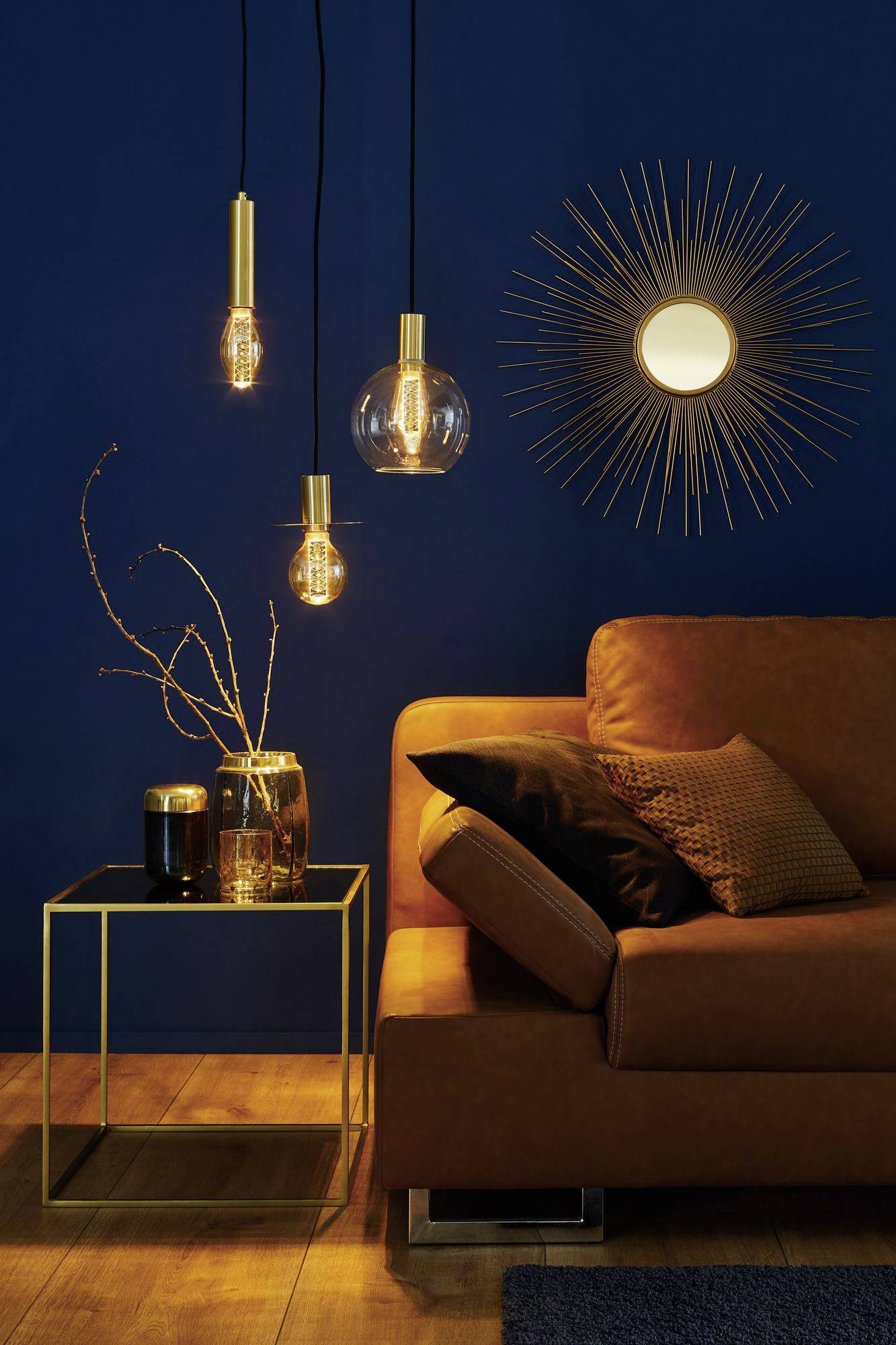 Štýlovo zariadená obývačka s hnedou sedačkou, modernými závesnými svietidlami a slnečným zrkadlom na tmavo modrej stene.