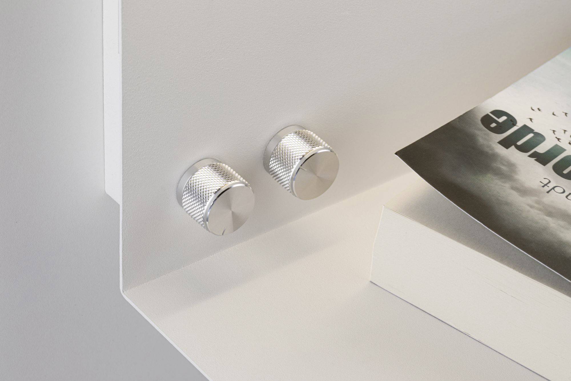 Dva strieborné gombíky na bielom povrchu vedľa čiastočne viditeľnej knihy.