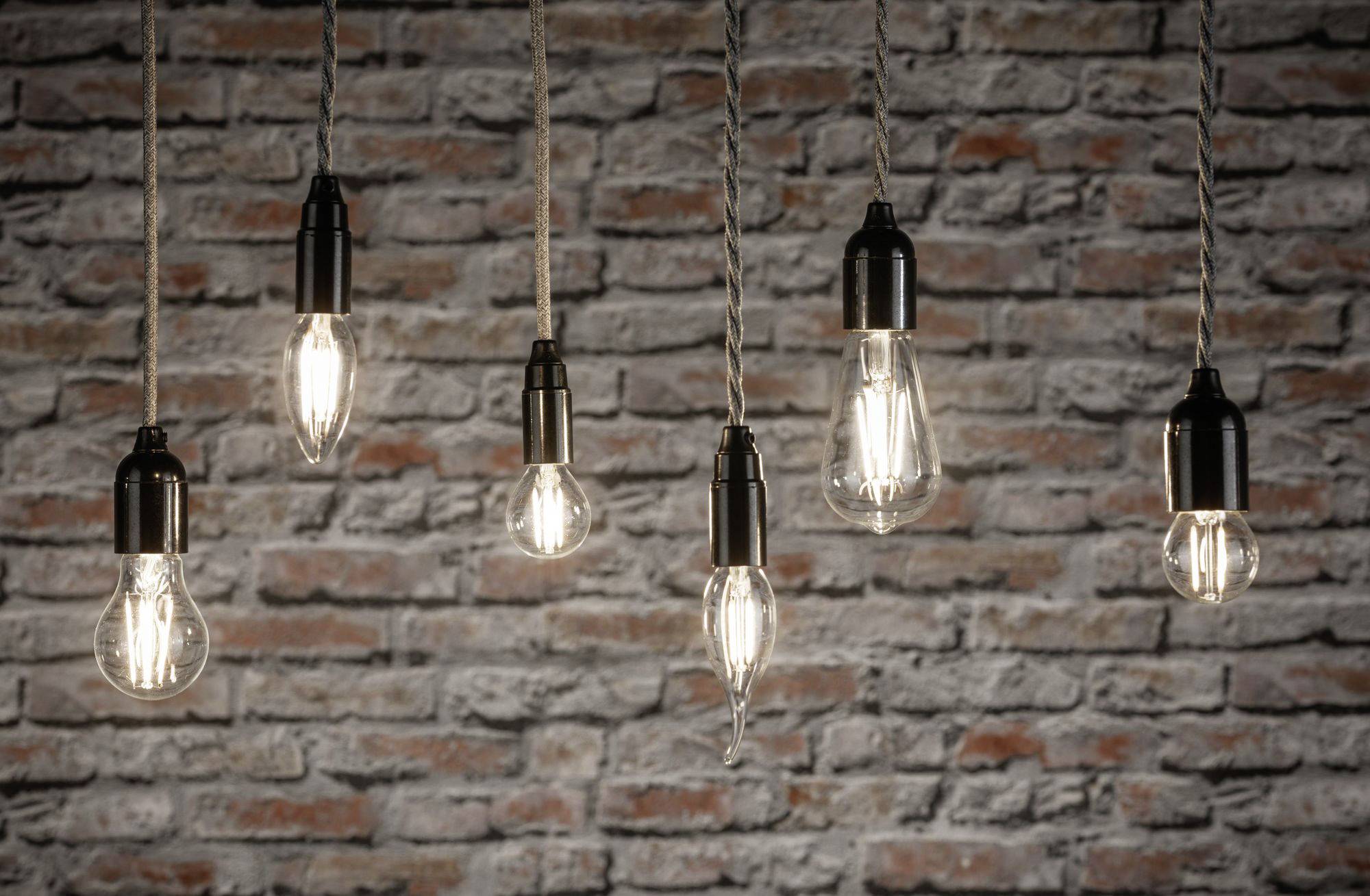 Šesť visiacich žiaroviek pred tehlovou stenou slabo svieti a vytvára rustikálnu, útulnú atmosféru.
