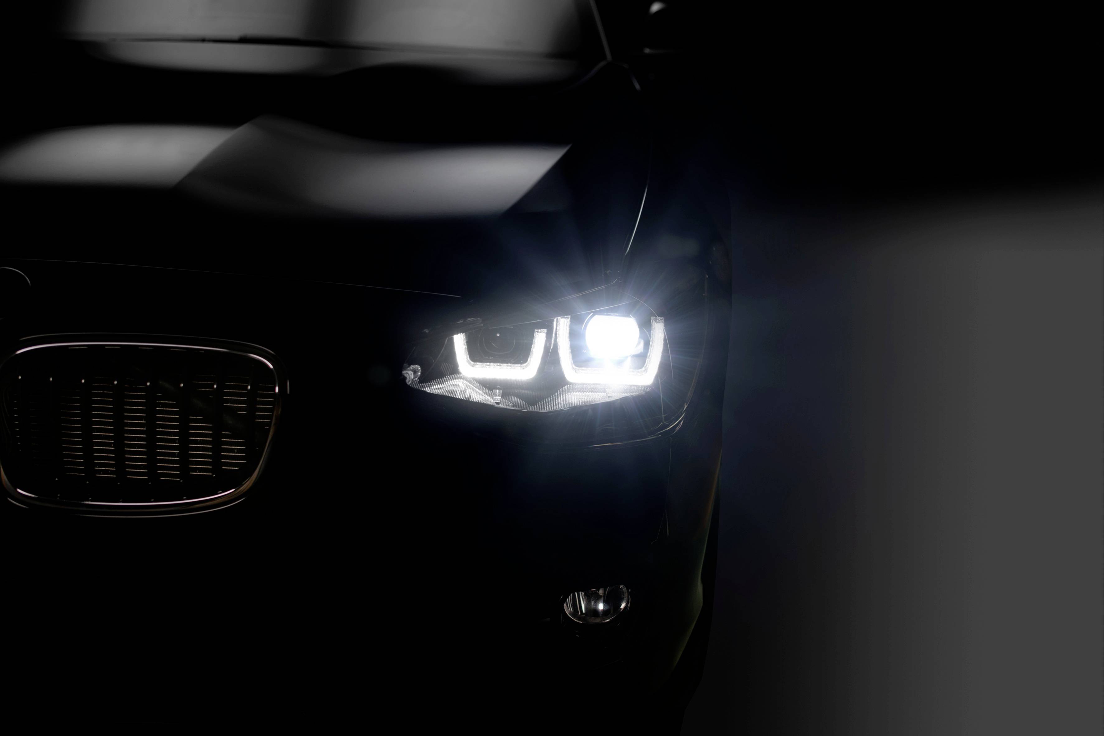 Tmavé auto spredu so zapnutým svetlometom, ktorý osvetľuje prednú časť vozidla.