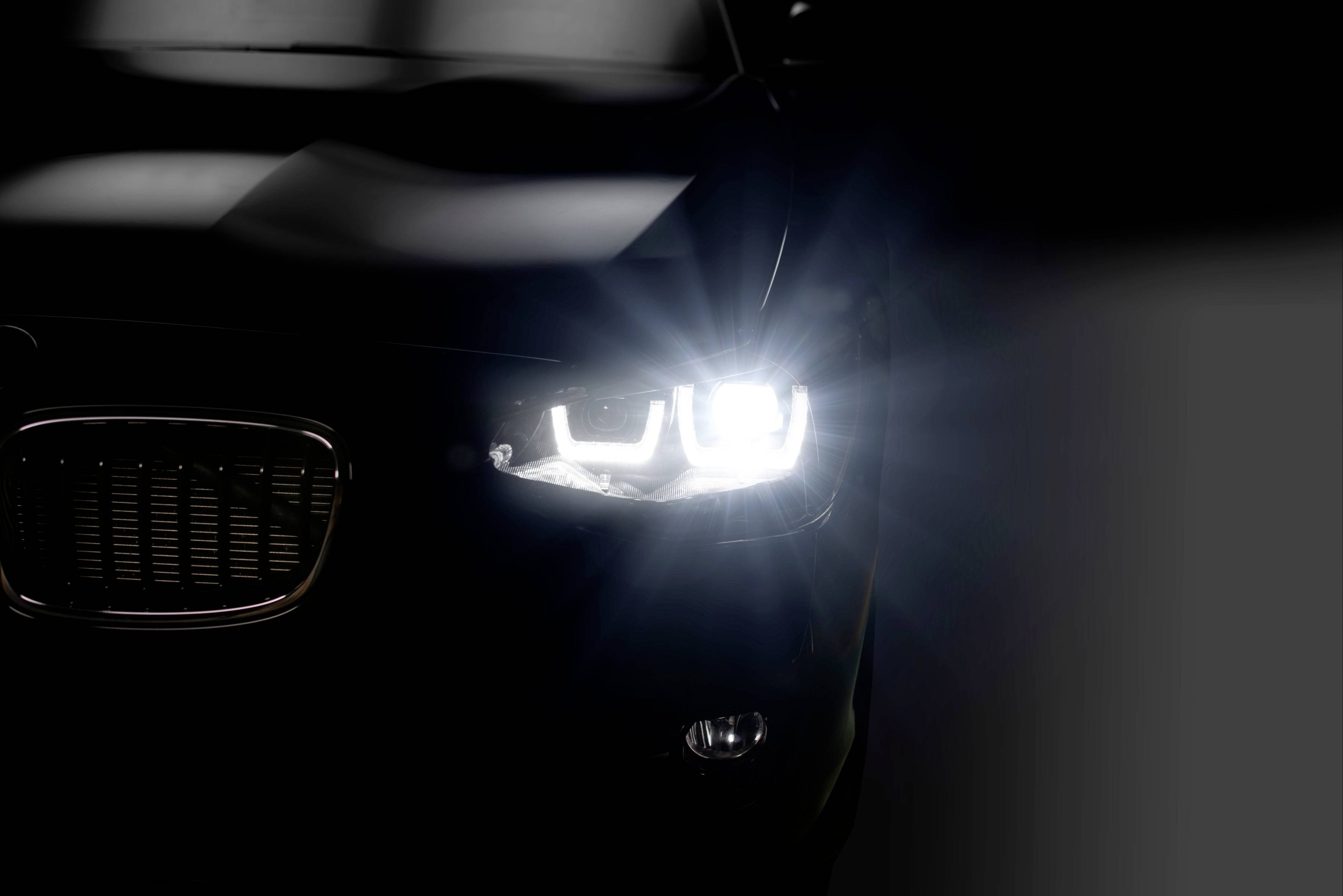 Detailný záber auta v noci so zapnutým svetlometom, osvetľujúcim cestu.