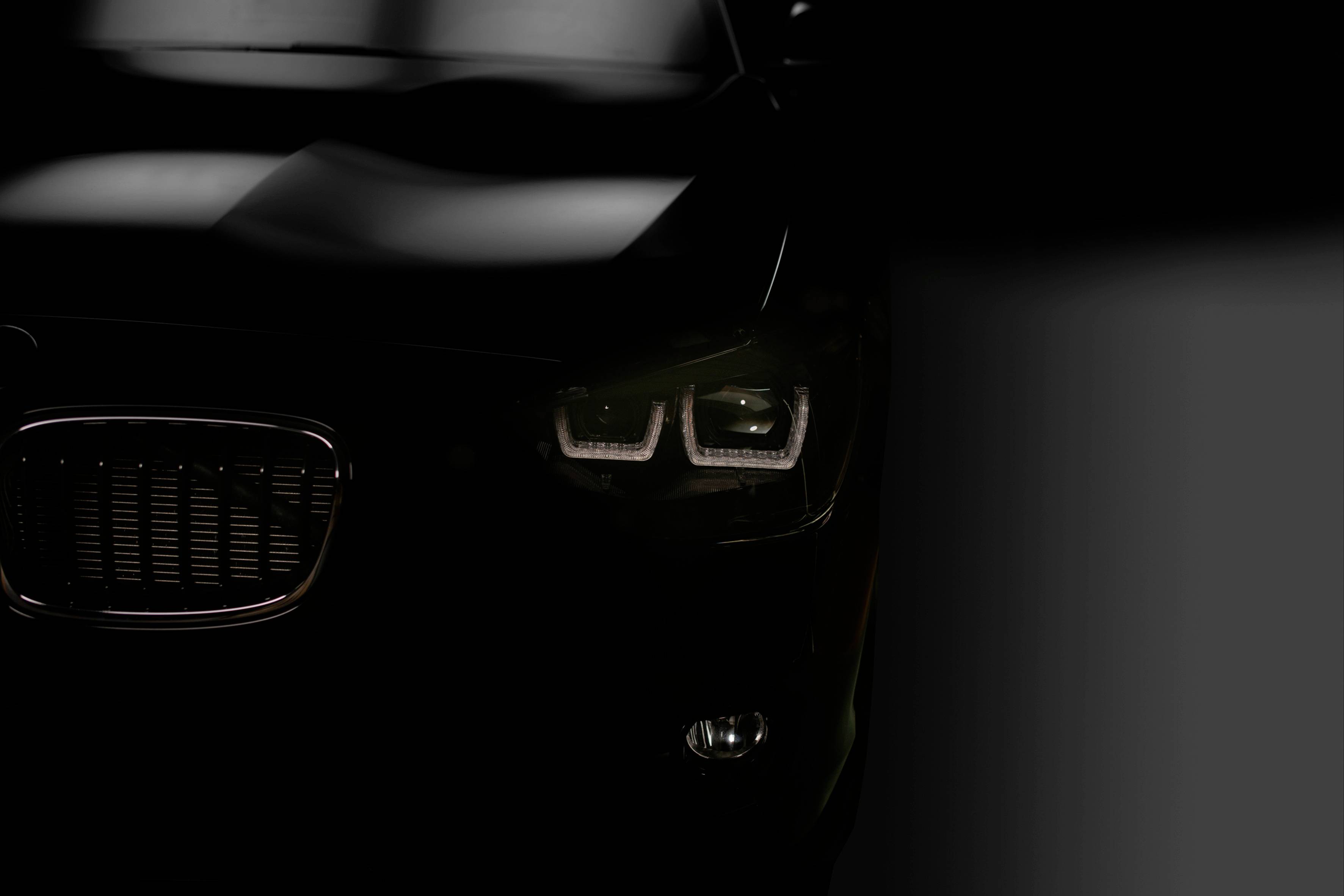 Automobil v tmavom prostredí zobrazuje prevažne prednú časť s výraznými svietiacimi svetlometmi a čiastočne viditeľnou chladičovou mriežkou.