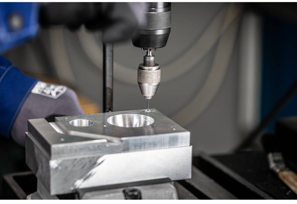 Osoba vŕta dieru do kovu pomocou vŕtačky a pritom má na rukách špeciálne pracovné rukavice.