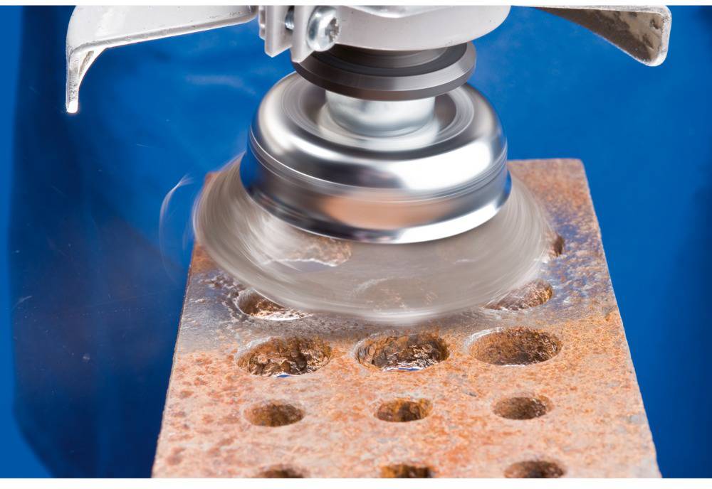 Drôtená kefa čistí hrdzavý kovový povrch s dierami. Pracovný postup v prostredí dielne.