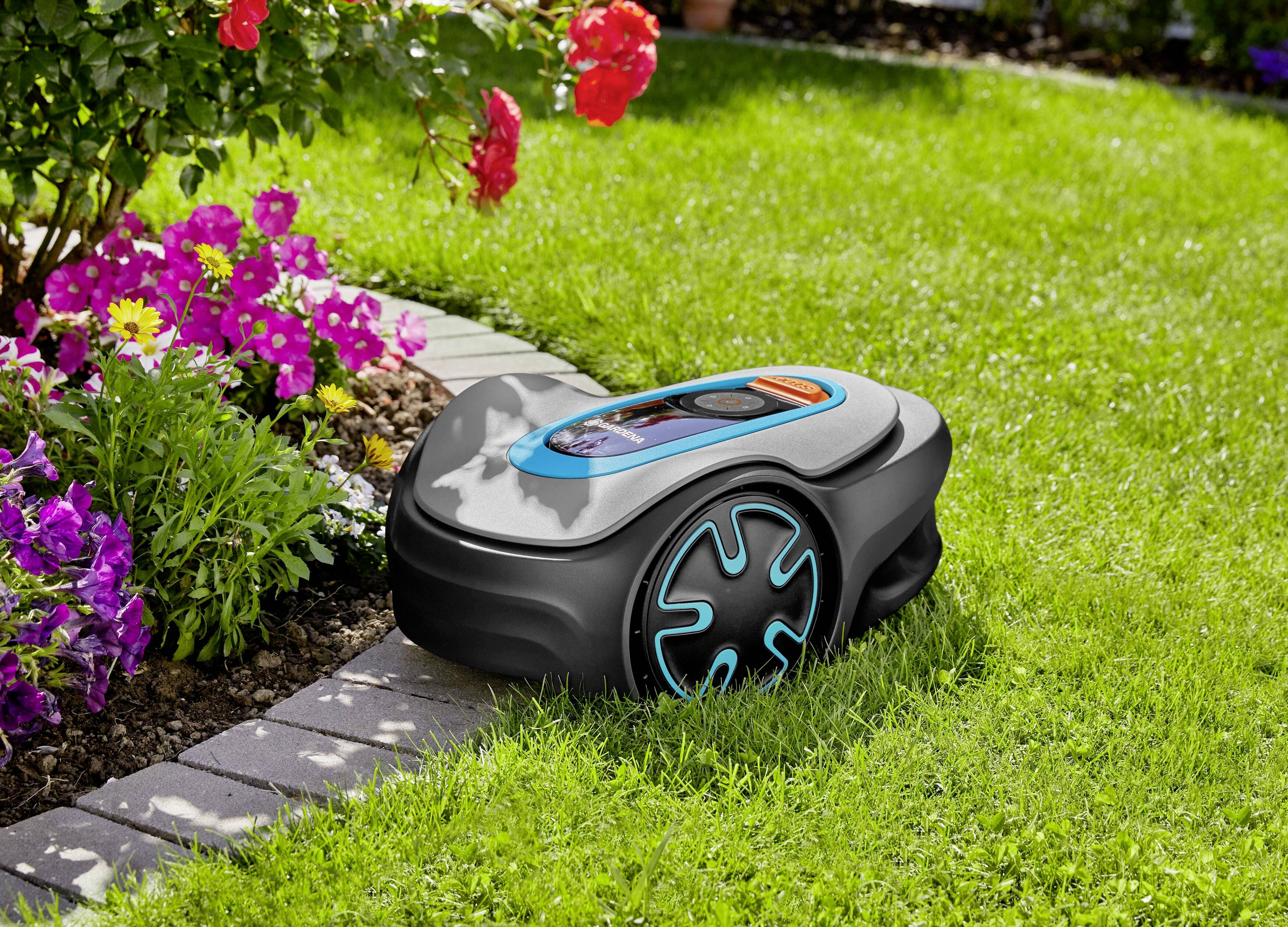 Autonómny robotický kosačkár kosí zelenú trávnatú plochu vedľa záhonu s farebnými kvetmi vrátane červených a fialových kvetov.