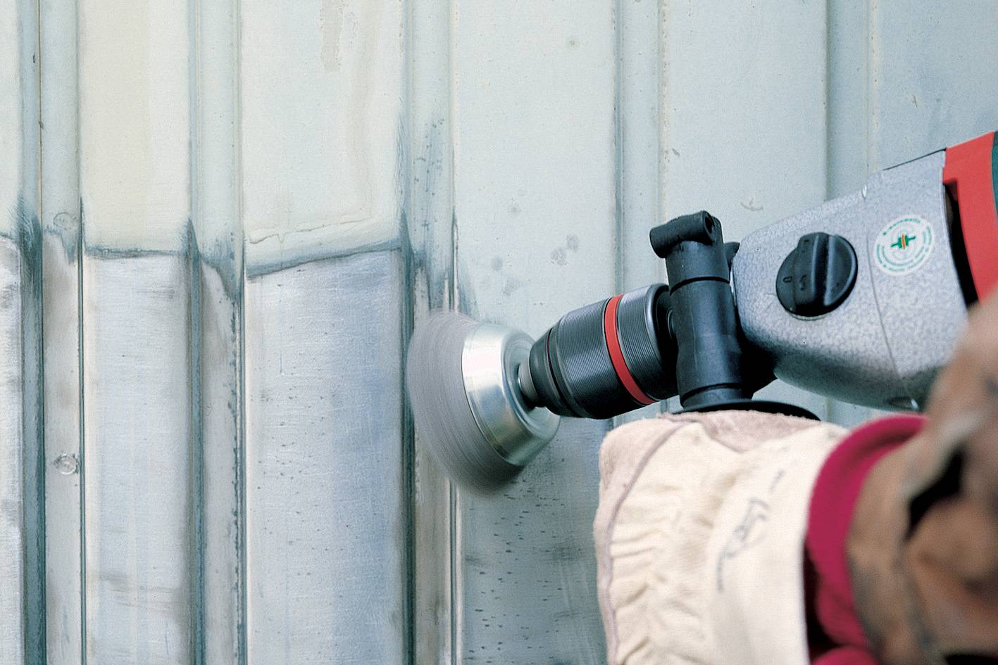 Jedna osoba brúsi pomocou stroja hrdzu z kovovej plochy. Brúsny kotúč odstraňuje nečistoty a zanecháva lesklý kov.