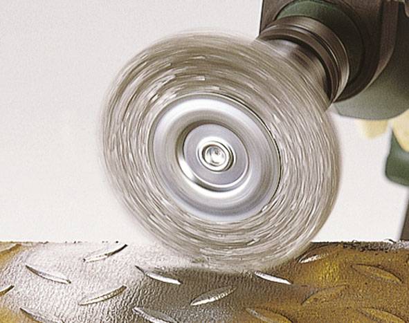 Rotujúca drôtená kefa leští kovový povrch, pričom sú viditeľné iskry.