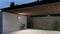 Moderný prístrešok z dreva a betónu s bicyklom pripevneným na stene a dvoma malými stromami v pozadí.
